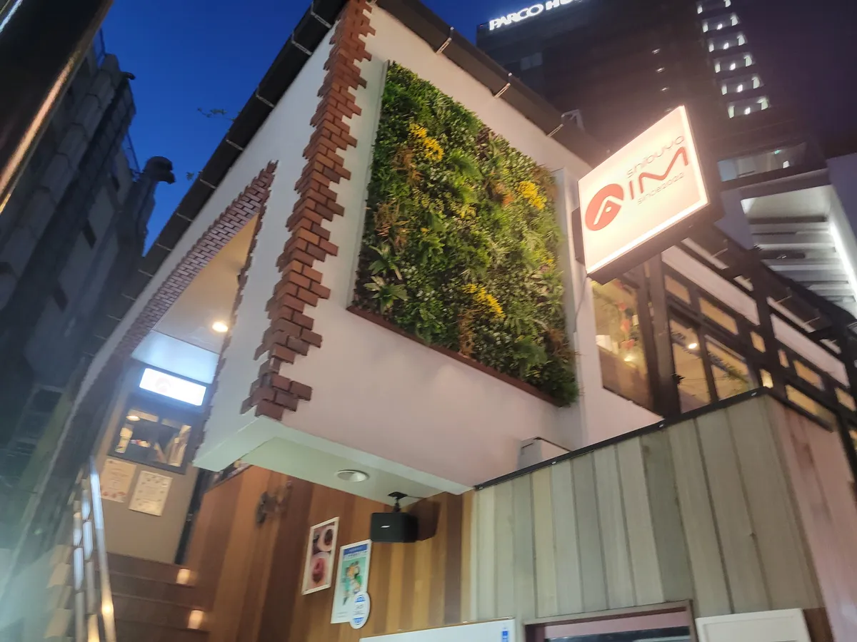 夕暮れの外観。緑の壁とAIMの看板、2階へのぼる階段